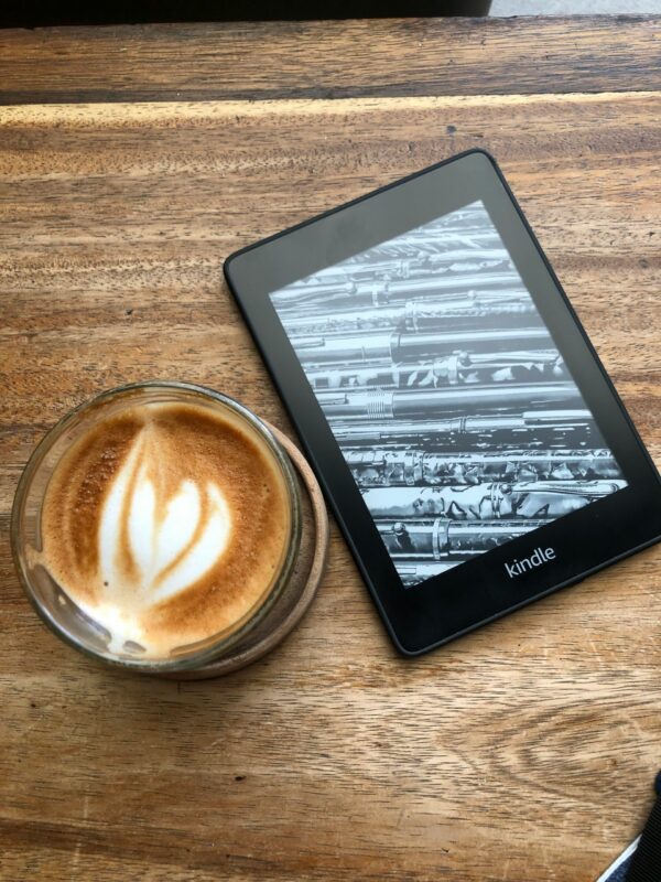 A Kindle resting on a wooden table beside a latte