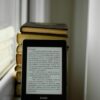 A Kindle propped against a stack of books on a windowsill