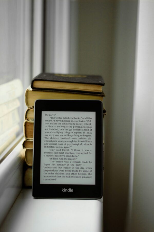 A Kindle propped against a stack of books on a windowsill