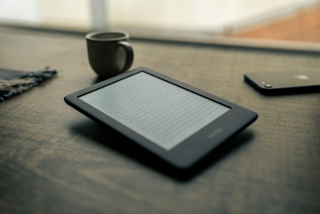 A Kindle e-reader resting on a wooden desk beside a cup of coffee