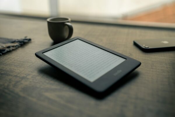A Kindle e-reader resting on a wooden desk beside a cup of coffee